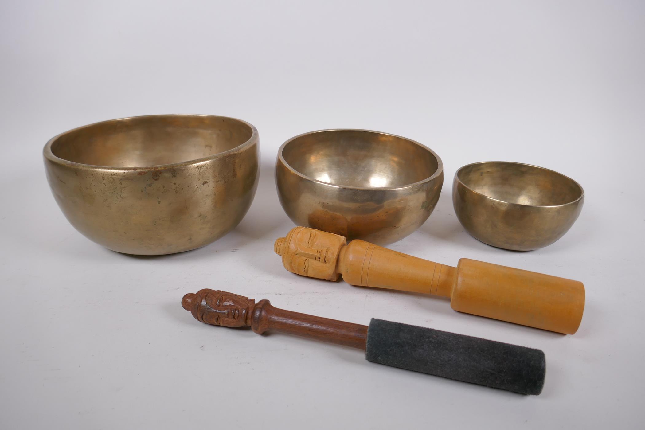 Three Tibetan graduated polished bronze singing bowls with hammered finish, and two wood hammers,