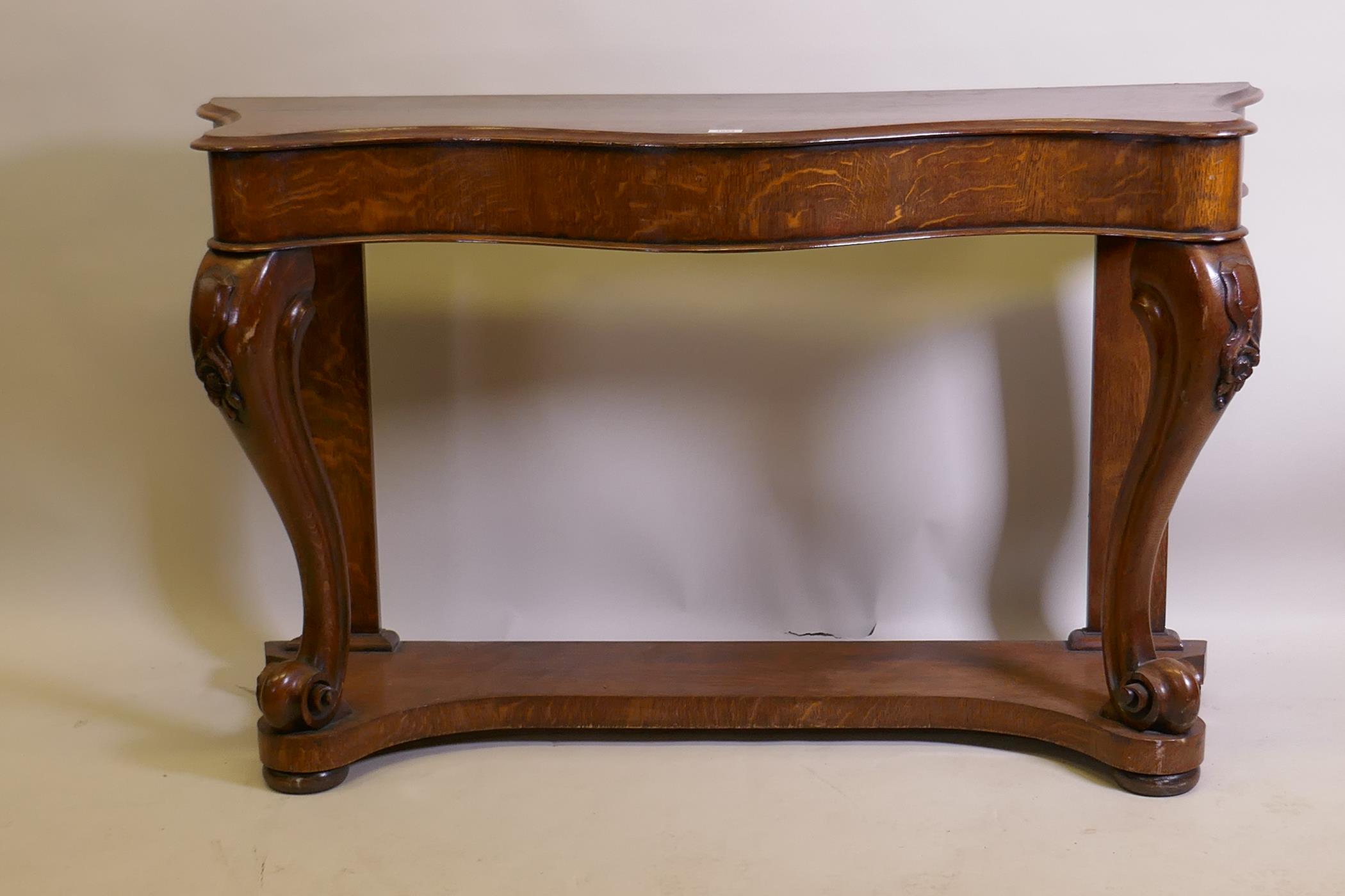 A Victorian oak serpentine console table on carved scrolled cabriole supports united by an under