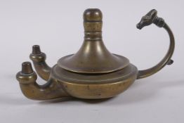 An antique brass twin spout whale oil lamp with animal mask decoration to handle, 15cm long