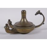 An antique brass twin spout whale oil lamp with animal mask decoration to handle, 15cm long