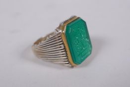 An Islamic white metal ring set with a carved green stone seal in a gilt metal mount, marks to