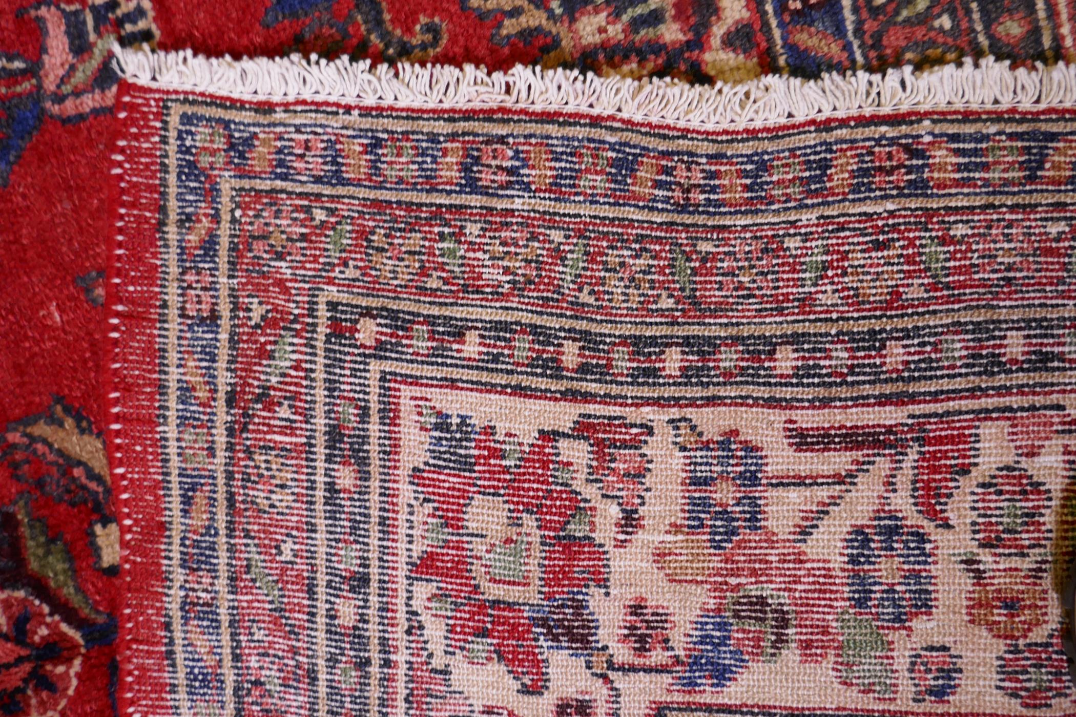 A Persian full pile red ground hand woven Sarouk village carpet with a floral medallion pattern - Image 6 of 6