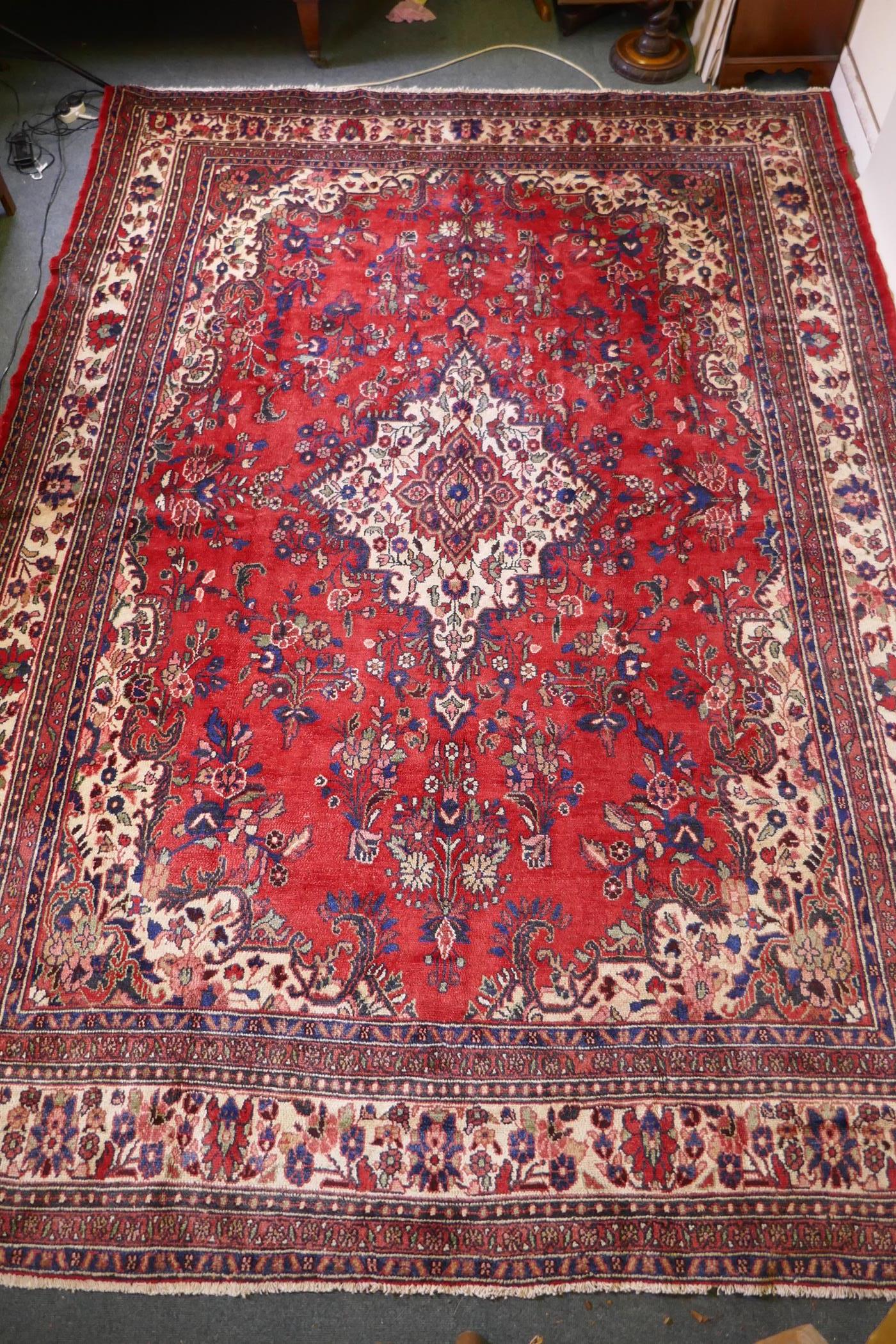 A Persian full pile red ground hand woven Sarouk village carpet with a floral medallion pattern