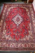 A Persian full pile red ground hand woven Sarouk village carpet with a floral medallion pattern