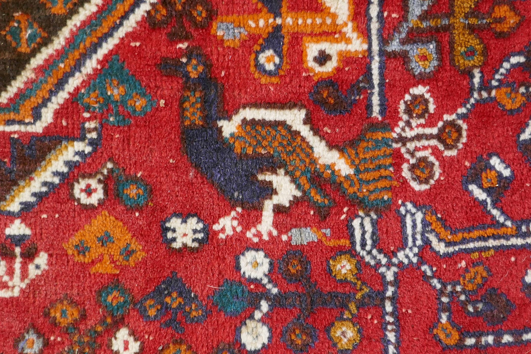 A hand woven red ground Persian carpet decorated with a geometric medallion, birds and camels, 158 x - Image 6 of 6