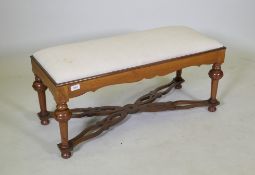 A walnut long stool with shaped frieze, raised on turned supports united by pierced shaped