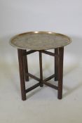 A Victorian brass top table with Japanese inspired decoration, on a folding wood base, 59 dia. x