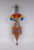 An African carved and brightly painted wood wall mask with a wading bird surmount, 67cm long