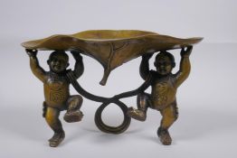 A Chinese bronze trinket bowl in the form of a lily pad held aloft by children, 15cm high x 25cm