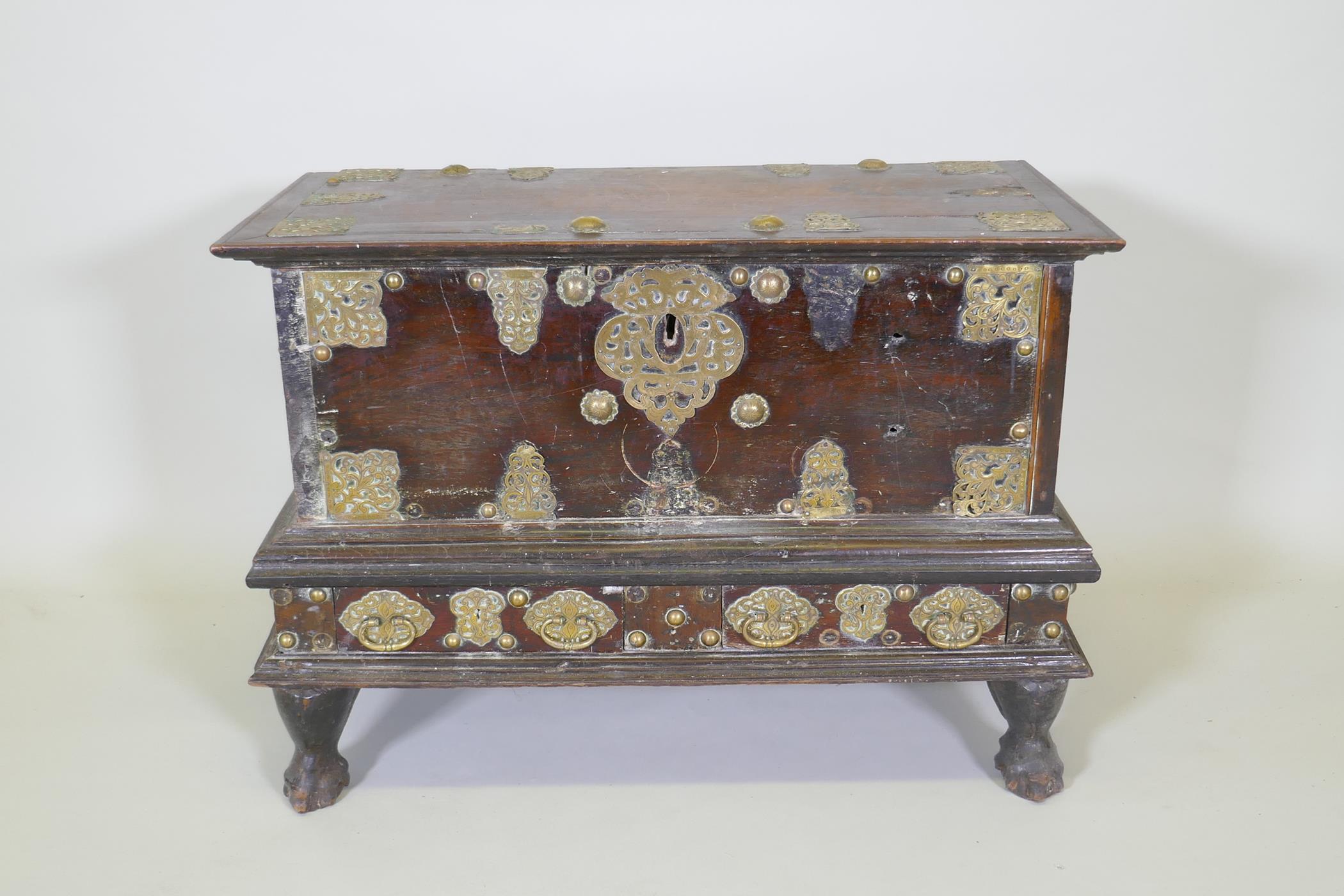 An C18th Dutch colonial teak chest with brass mounts, lift up top and two drawers, raised on claw