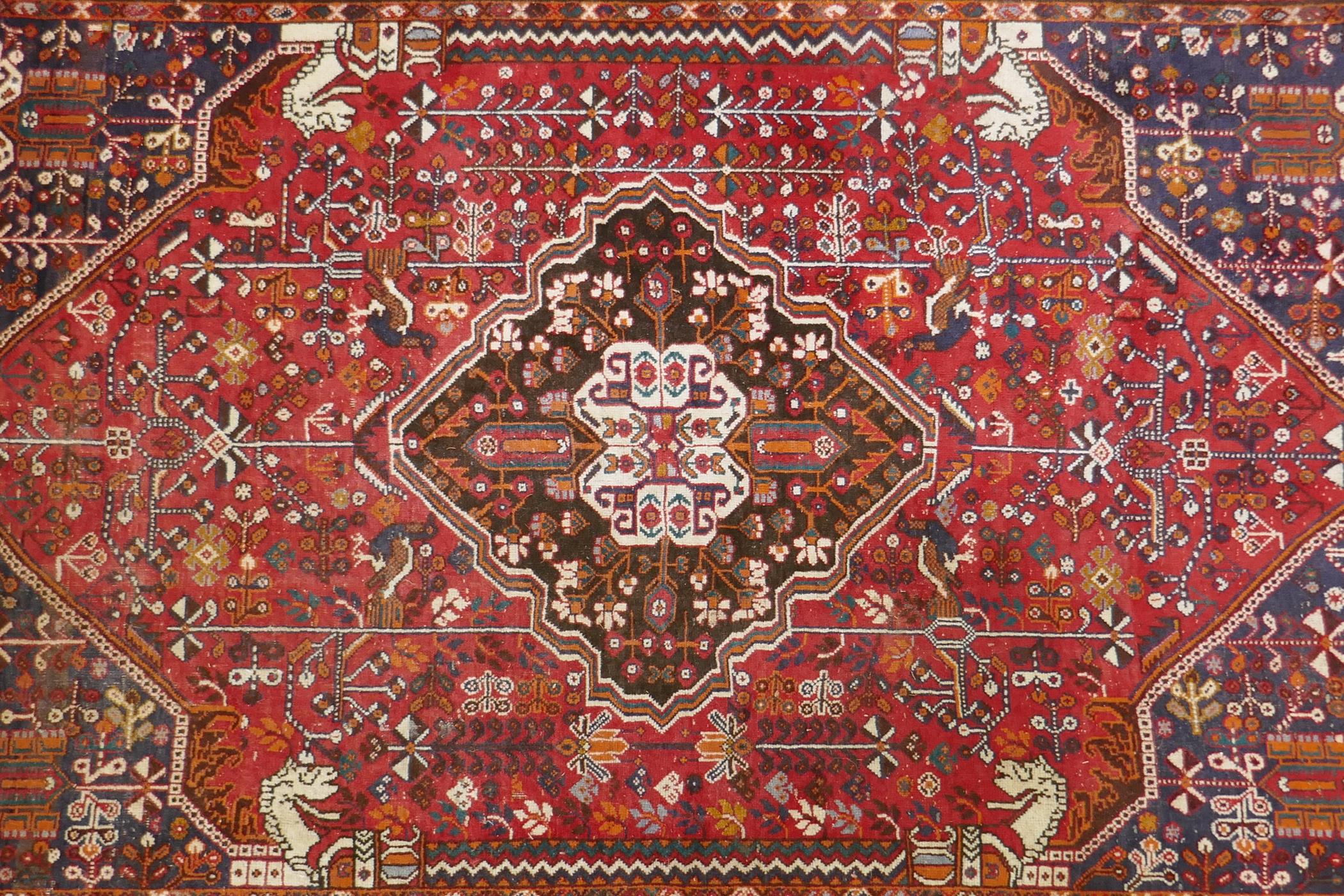 A hand woven red ground Persian carpet decorated with a geometric medallion, birds and camels, 158 x
