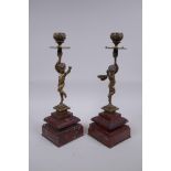 A pair of Victorian bronze candlesticks in the form of a winged putti, on red marble bases, 28cm