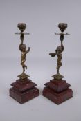 A pair of Victorian bronze candlesticks in the form of a winged putti, on red marble bases, 28cm