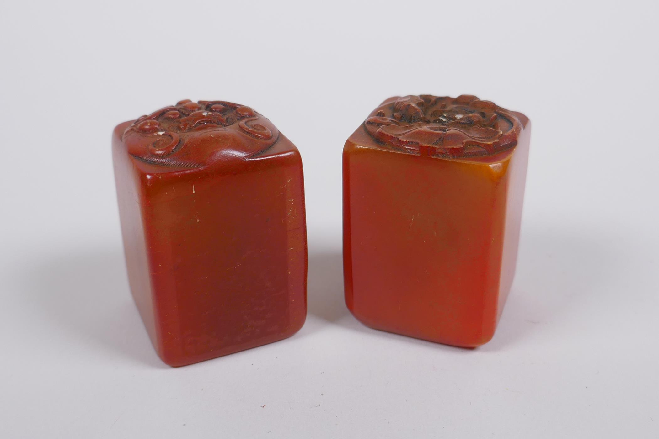 A pair of Chinese amber soapstone seals with dragon mask and lotus pad decoration, 3 x 3cm, 4cm high