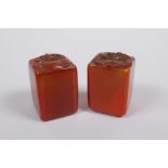 A pair of Chinese amber soapstone seals with dragon mask and lotus pad decoration, 3 x 3cm, 4cm high