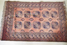 A vintage faded red hand woven wool Bokhara carpet with geometric designs, 130 x 210cm