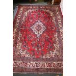 A Persian full pile red ground hand woven Sarouk village carpet with a floral medallion pattern