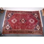 A hand woven red ground Persian carpet with a unique medallion design and chocolate brown borders,