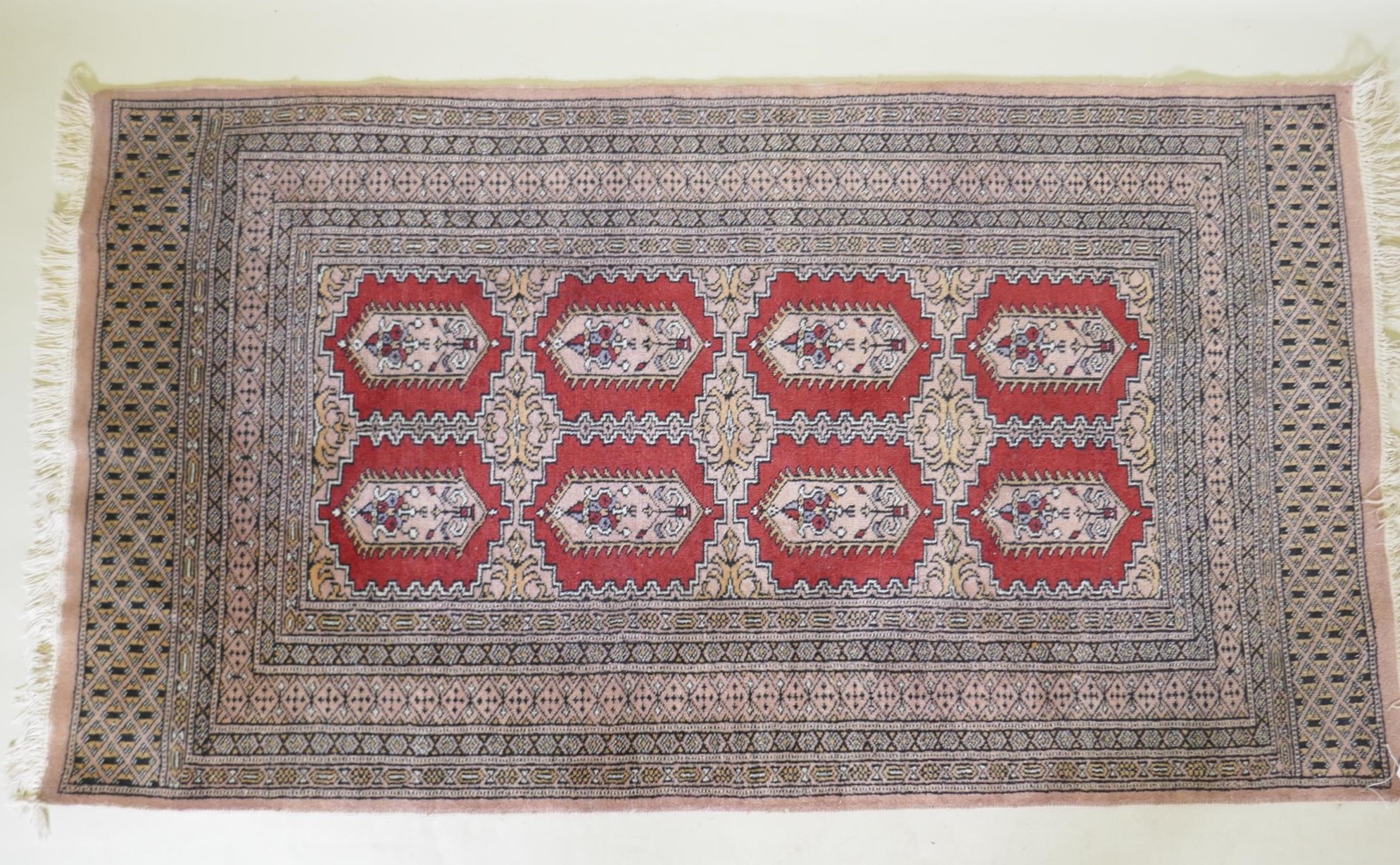 A hand woven wool Bokhara rug, medallion design on a pink ground, 94 x 150cm