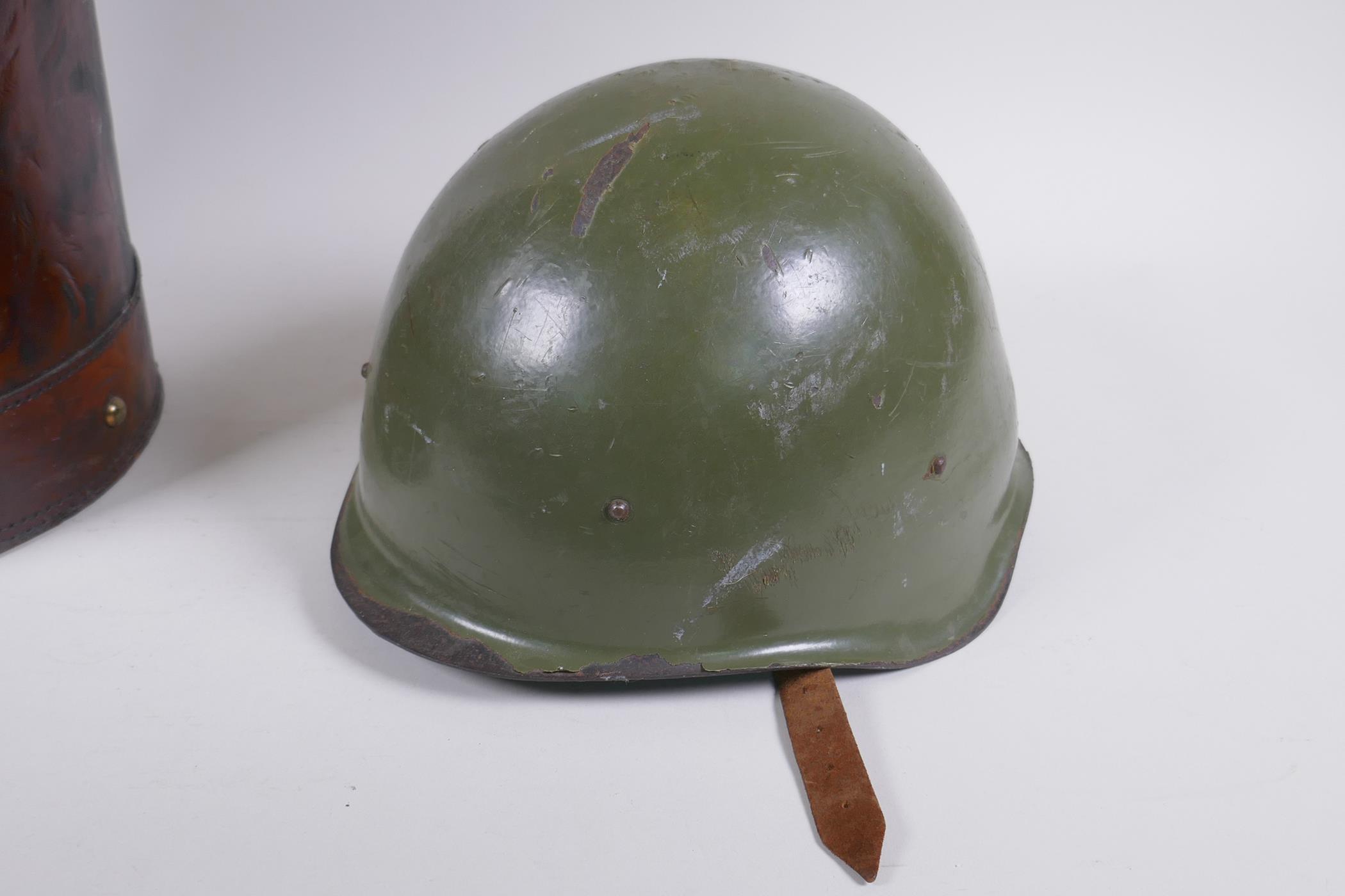 A vintage leather shell case decorated with a later applied armorial crest, and a steel military - Image 4 of 5