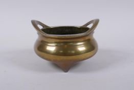 An antique Chinese polished bronze censer with two phoenix eye handles and tripod supports,