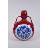 A Chinese sang de boeuf porcelain two handled flask with blue and white floral decorative panels,