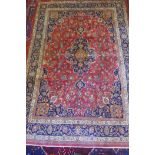 A washed red ground Persian Mashad carpet with traditional floral medallion design, signed by the