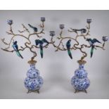 A pair of polychrome porcelain and gilt metal three branch candlesticks, decorated with birds