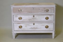 An antique painted and distressed pine commode, with three long drawers, canted corners and raised