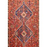 An antique Persian wool rug, with twin blue ground medallions on a tomato field, 124 x 92cm