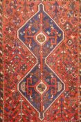 An antique Persian wool rug, with twin blue ground medallions on a tomato field, 124 x 92cm