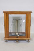 A set of balance scales in a glazed wood cabinet, 43 x 30 x 50cm