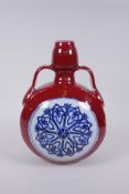 A Chinese sang de boeuf porcelain two handled flask with blue and white floral decorative panels,