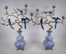 A pair of polychrome porcelain and gilt metal three branch candlesticks, decorated with birds