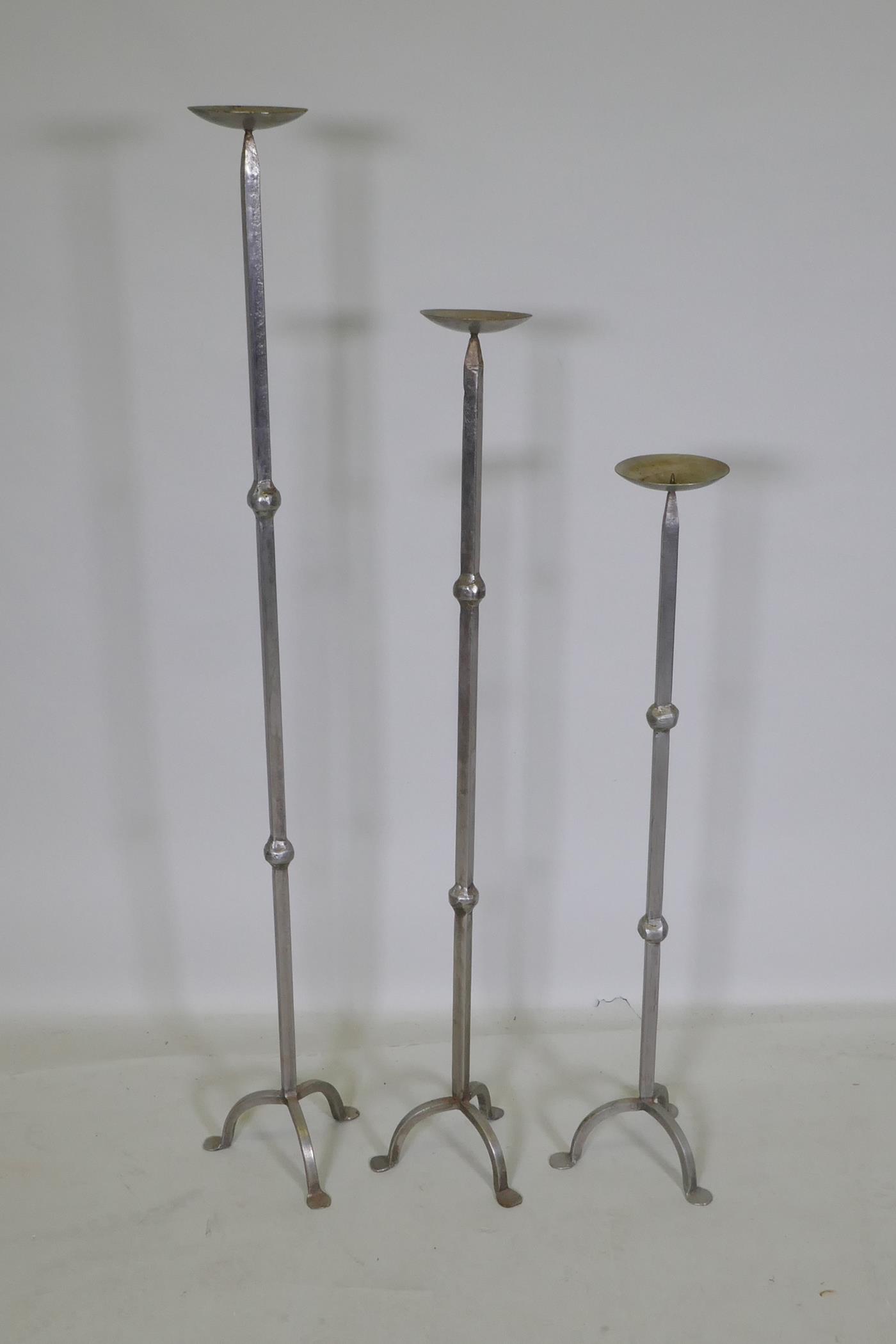 Three graduated wrought metal pricket candlesticks, largest 113cm