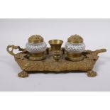 An antique brass desk stand with raised vine decoration and two glass inkwells, 30 x 20cm