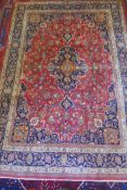 A washed red ground Persian Mashad carpet with traditional floral medallion design, signed by the