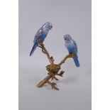 A gilt metal tea light holder in the form of a tree branch with two polychrome porcelain birds