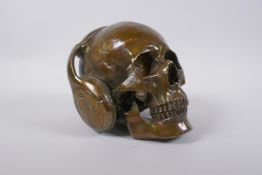 A bronzed metal ornamental skull wearing headphones, 16cm high