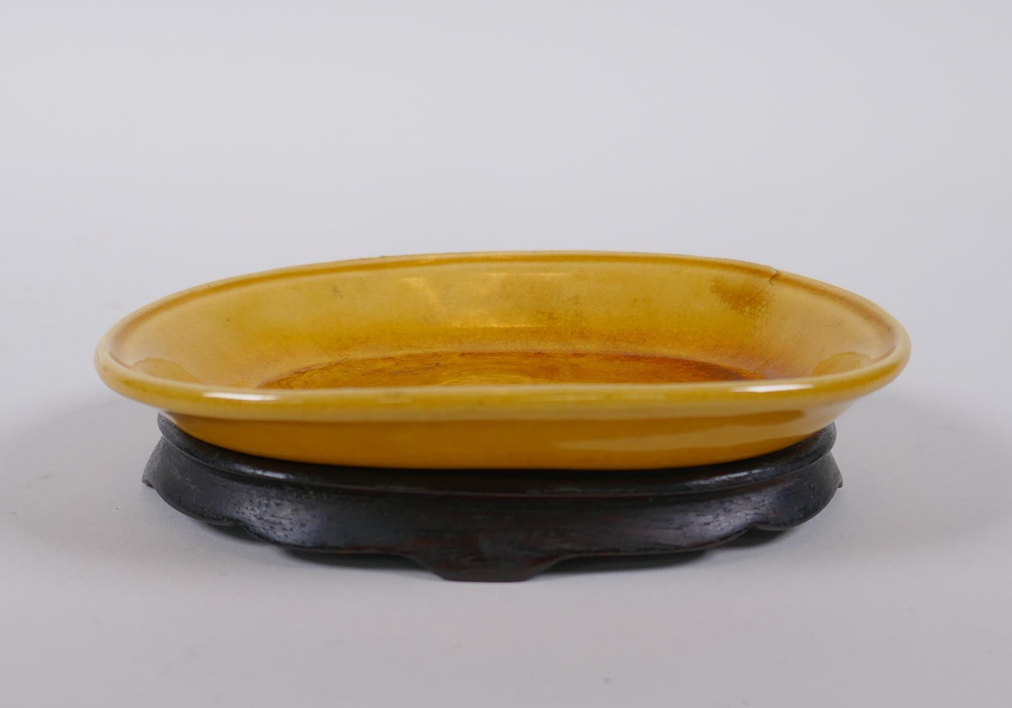 A Chinese yellow ground porcelain dish with incised dragon decoration, on a hardwood stand, 12 x 9cm