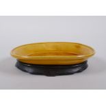 A Chinese yellow ground porcelain dish with incised dragon decoration, on a hardwood stand, 12 x 9cm