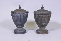A pair of antique cast iron fluted urns and covers with mask decoration, 30cm high