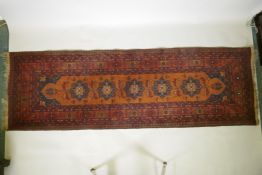 An antique oriental red ground wool runner decorated with geometric floral medallions and birds,
