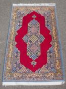A full pile fine hand woven Iranian rug, signed and dated, with age, red ground with blue borders