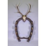 A Victorian oak gun rack in the form of horse shoe with deer's hoof hooks and antler crest, 84cm