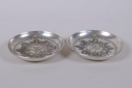 A pair of Chinese white metal trinket dishes with raised decoration of the eight immortals, mark