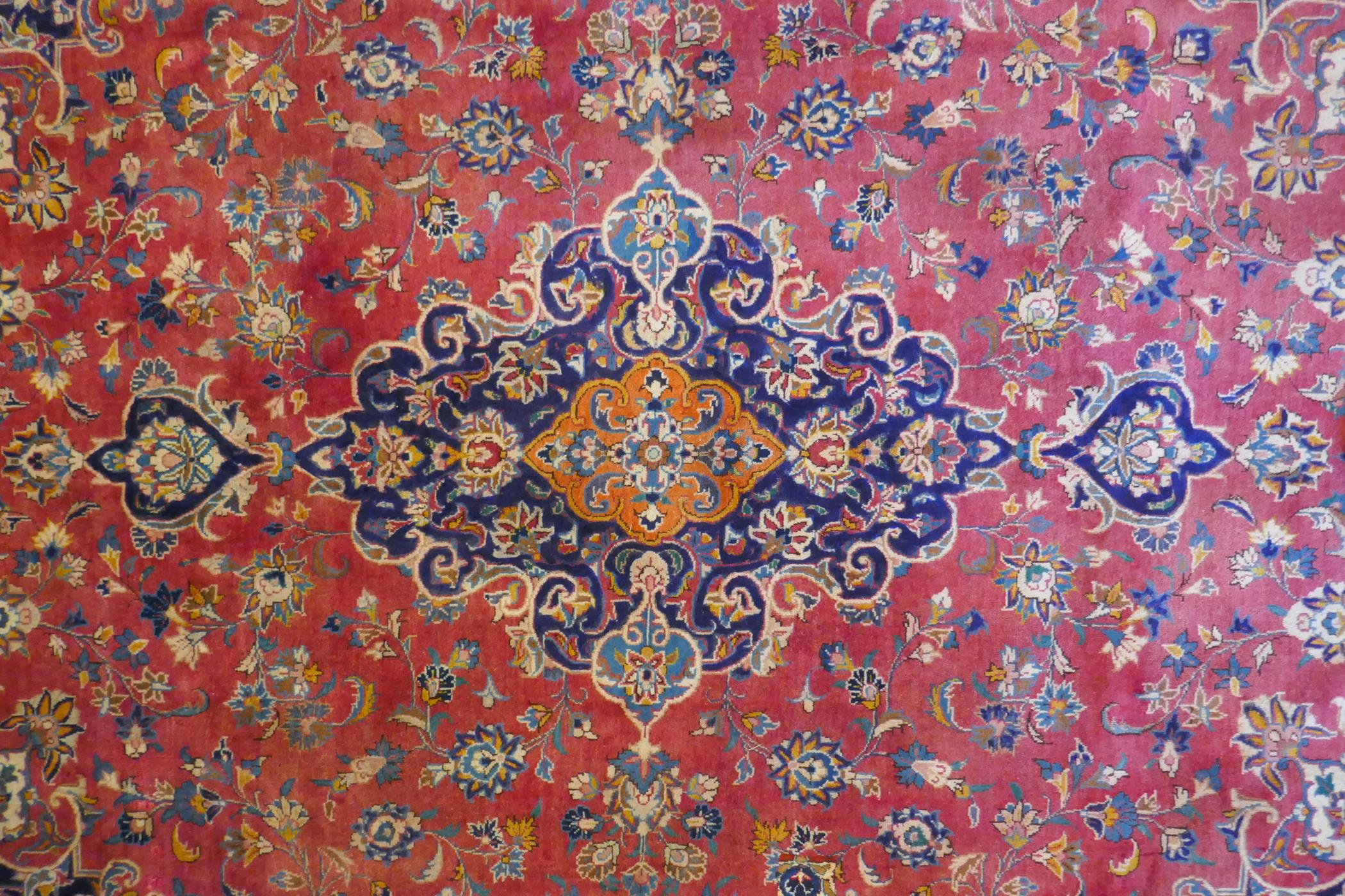 A washed red ground Persian Mashad carpet with traditional floral medallion design, signed by the - Image 3 of 8