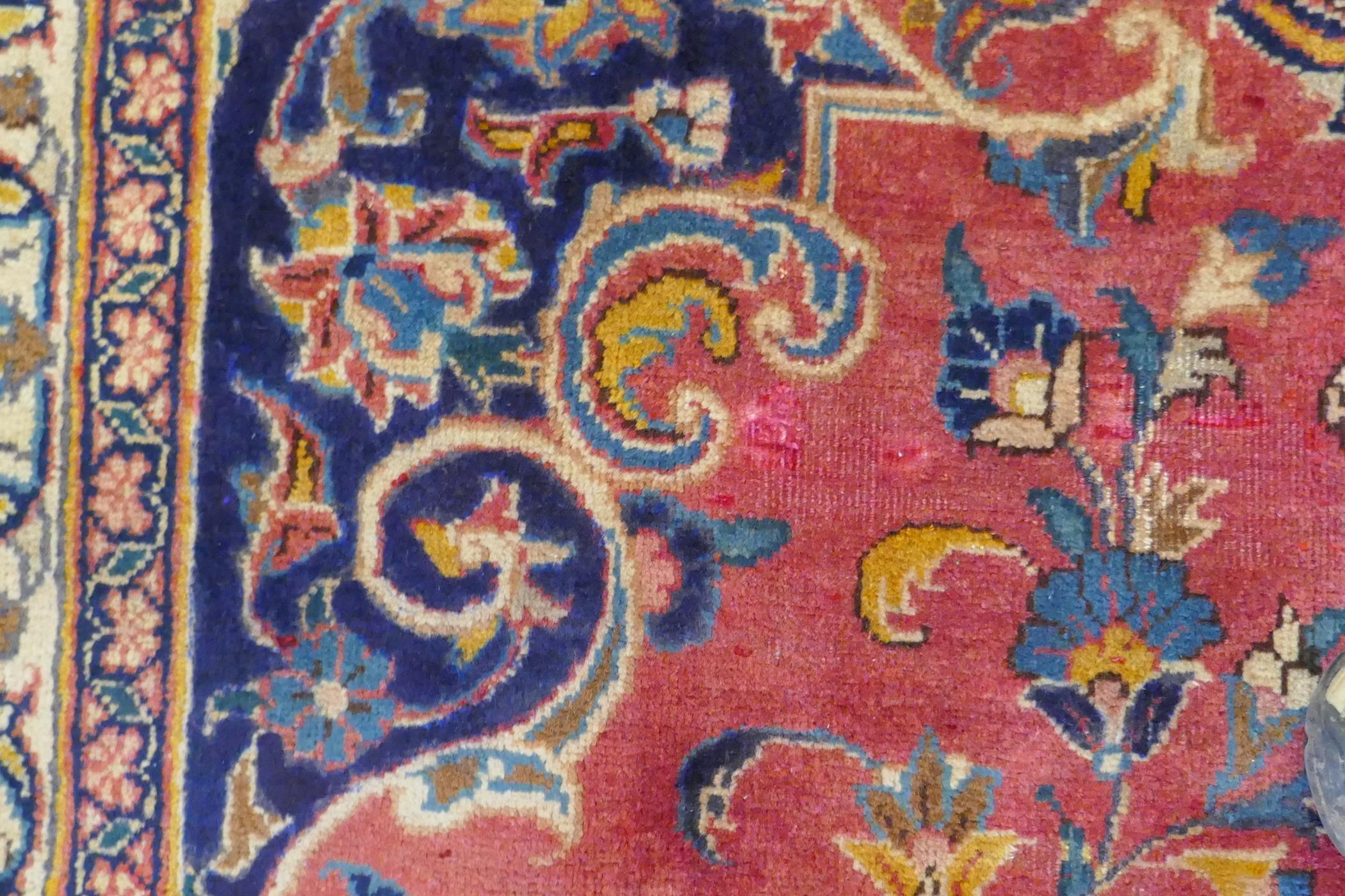 A washed red ground Persian Mashad carpet with traditional floral medallion design, signed by the - Image 5 of 8