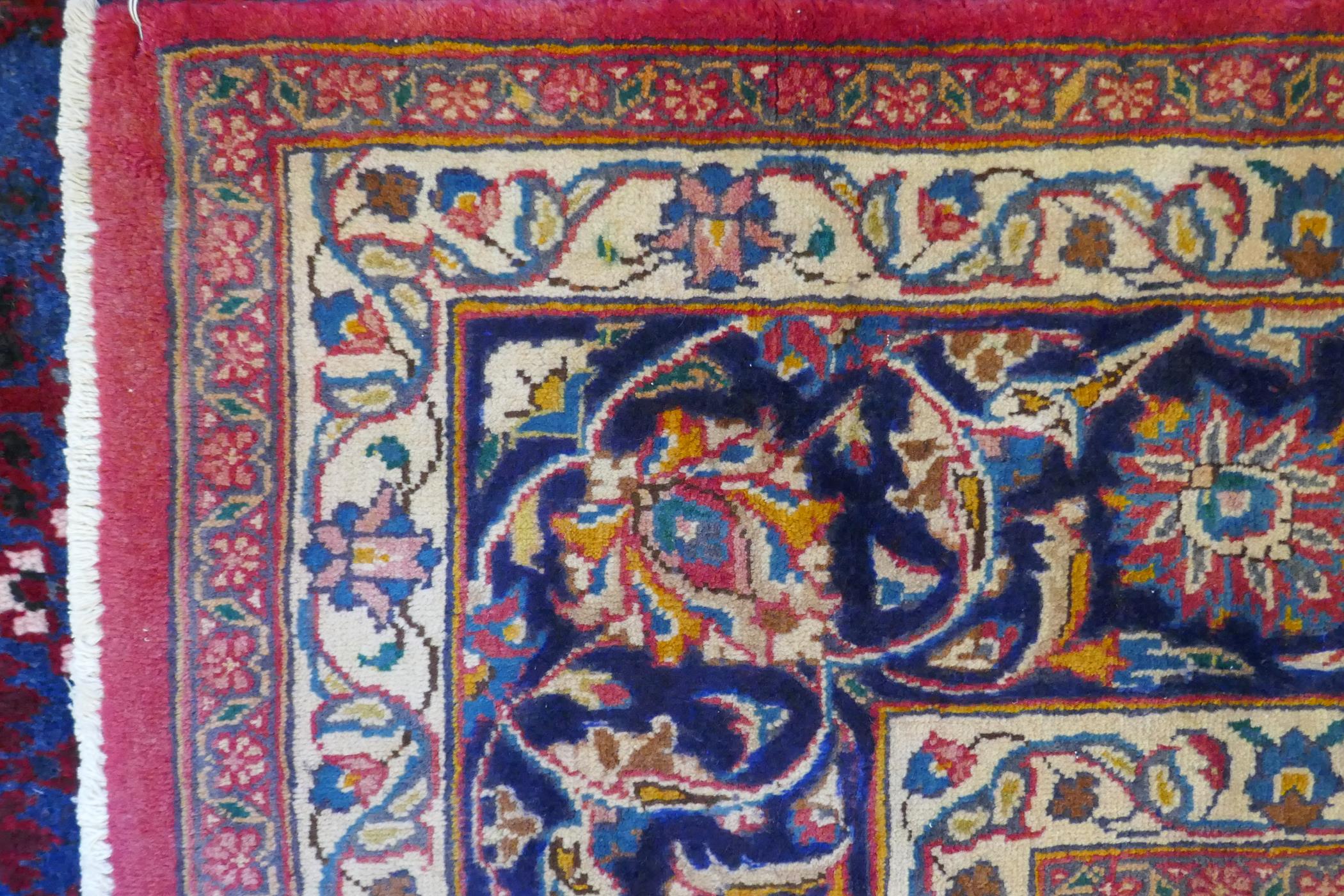 A washed red ground Persian Mashad carpet with traditional floral medallion design, signed by the - Image 7 of 8