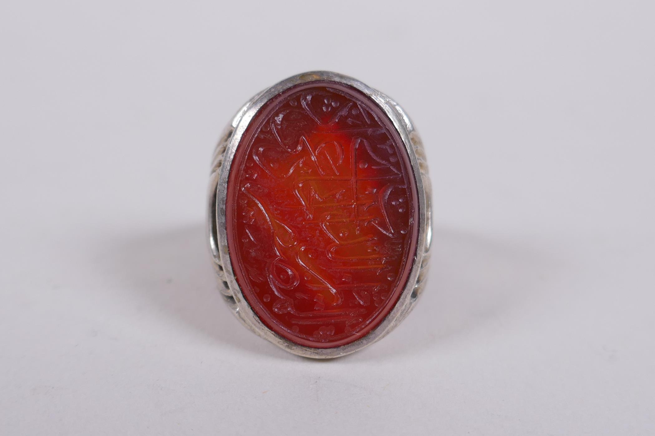 An Islamic white metal ring set with an agate intaglio seal, carved with Islamic script, marks to